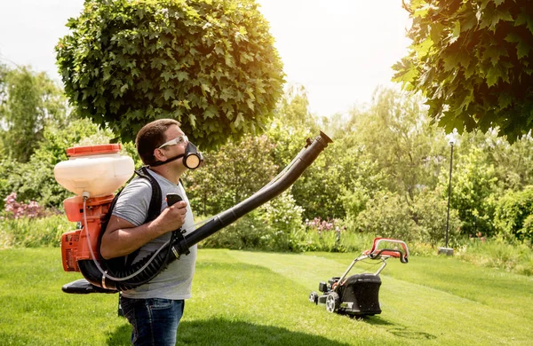 Giardiniere in maschera protettiva e occhiali spruzzando pesticidi tossici alberi — Foto Stock