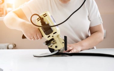 Kadın işçi elektrikli kumaş kesim makinesi kullanıyor. Kumaş endüstrisi üretimi