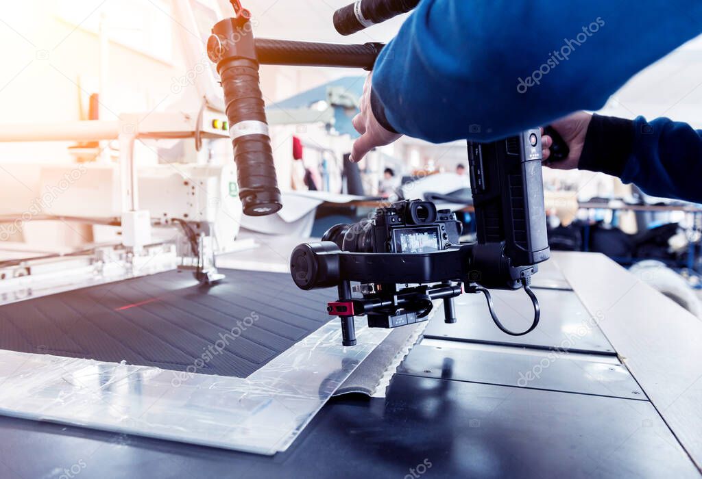 Videographer using stadicam, making video of machine at sew factory