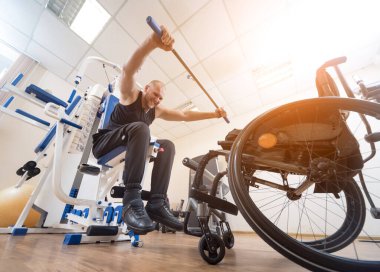 Tekerlekli sandalyeden ayrı olarak egzersiz yapan engelli bir adam..