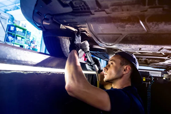 Car mechanic examining car suspension of lifted automobile at service station