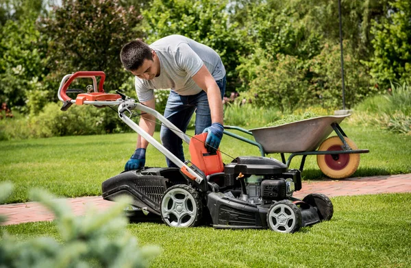 Trädgårdsmästare tömma gräsklippare gräs i en skottkärra efter klippning. — Stockfoto