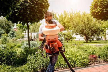 Koruyucu maskeli bir bahçıvan ve zehirli böcek ilaçları sıkan bardaklar.
