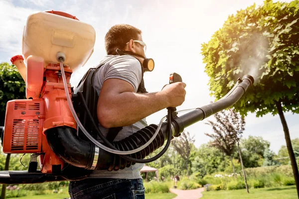 Giardiniere in maschera protettiva e occhiali spruzzando pesticidi tossici alberi — Foto Stock