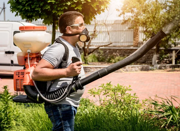 Giardiniere in maschera protettiva e occhiali spruzzando pesticidi tossici alberi — Foto Stock