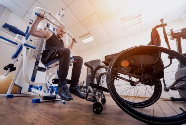 Tekerlekli sandalyeden ayrı olarak egzersiz yapan engelli bir adam..