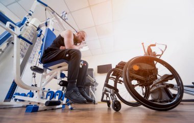 Tekerlekli sandalyeden ayrı olarak egzersiz yapan engelli bir adam..