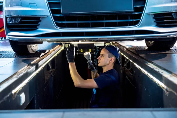 Car mechanic examining car suspension of lifted automobile at service station