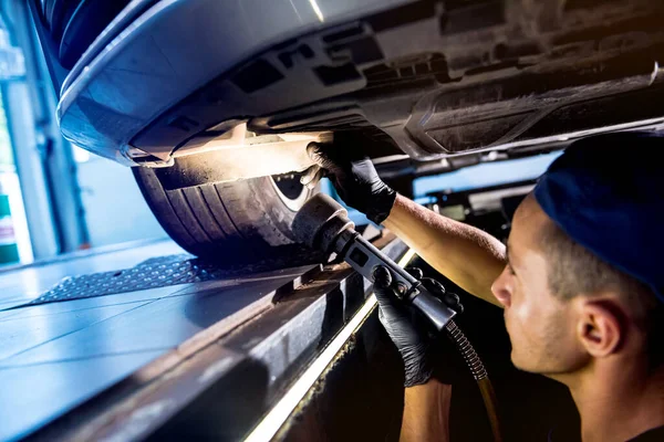 Car mechanic examining car suspension of lifted automobile at service station — Stock Photo, Image
