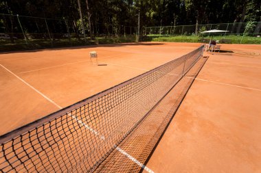 Tenis ağı kırmızı kil sahada çizgiler ve gölgelerle.