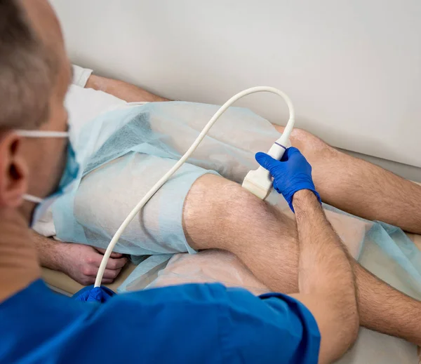 Doktorn gör ett ultraljud av mannens knä. — Stockfoto