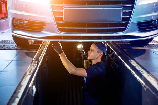 Car mechanic examining car suspension of lifted automobile at service station