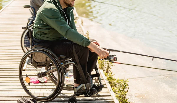 Joven hombre discapacitado en una silla de ruedas pesca. — Foto de Stock