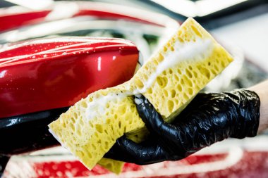 İşçi araba yıkamada kırmızı arabayı süngerle yıkıyor.