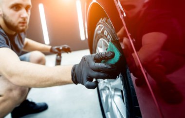 Araba servisi çalışanı mikro fiber bezle araba tekerleklerini parlatıyor..