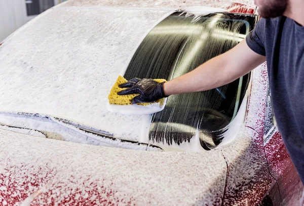 Trabajador lavando coche rojo con esponja en un lavado de coche — Foto de Stock