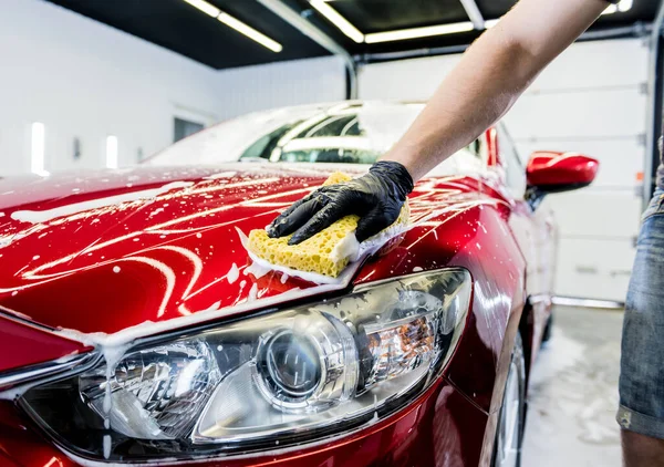 Trabajador lavando coche rojo con esponja en un lavado de coche —  Fotos de Stock