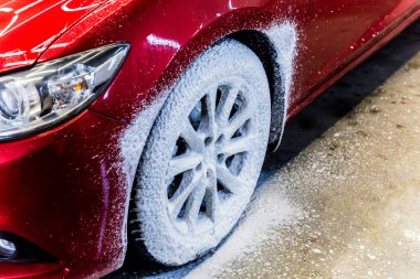 Araba tekerleğini fırça ve suyla temizliyorum.