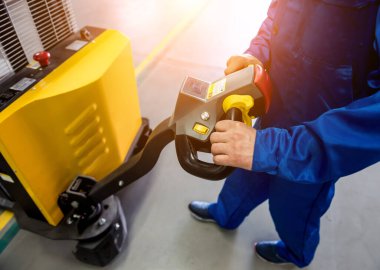 Depoda çalışan bir işçi paletleri taşımak için bir el paleti istifleyicisi kullanır..