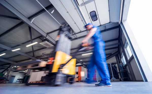 Um trabalhador em um armazém usa um empilhador de paletes de mão para transportar paletes. — Fotografia de Stock