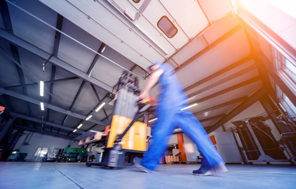 Um trabalhador em um armazém usa um empilhador de paletes de mão para transportar paletes. — Fotografia de Stock