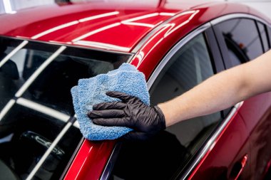 Araba servisi çalışanı mikrofiber bezle araba cilalıyor..
