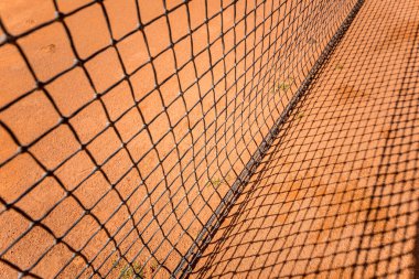 Tenis ağı kırmızı kil sahada çizgiler ve gölgelerle.