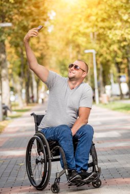Park sokağındaki tekerlekli sandalyedeki engelli adam akıllı telefon kullanıyor.