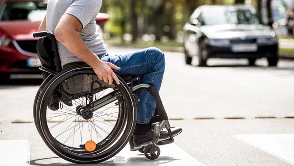 Tekerlekli sandalyedeki engelli adam caddeden karşıya geçiyor. — Stok fotoğraf