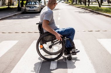 Tekerlekli sandalyedeki engelli adam caddeden karşıya geçiyor.