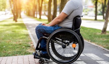 Tekerlekli sandalyedeki engelli adam yaya geçidinden karşıya geçmeye hazırlanıyor.