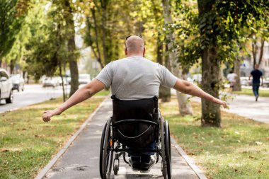 Tekerlekli sandalyedeki engelli adam parkta yürüyor.