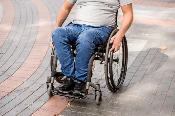 Tekerlekli sandalyedeki engelli adam parkta yürüyor.