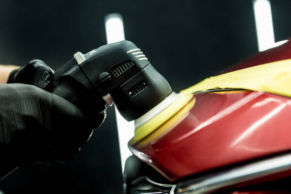 Car service worker polishes a car details with orbital polisher.