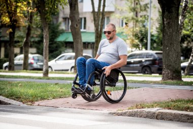 Tekerlekli sandalyedeki engelli adam caddeden karşıya geçiyor.