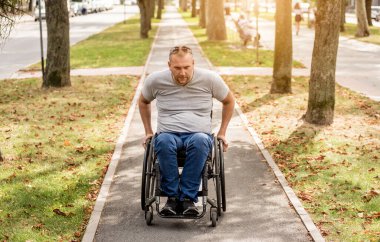 Tekerlekli sandalyedeki engelli adam parkta yürüyor.