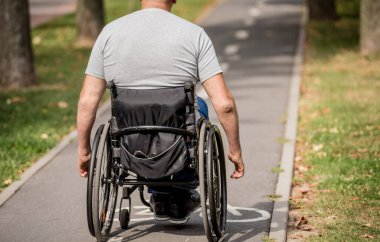 Tekerlekli sandalyedeki engelli adam parkta yürüyor.