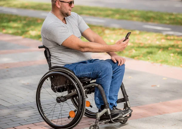 Handicapped man in wheelchair at the park alley use a smartphone