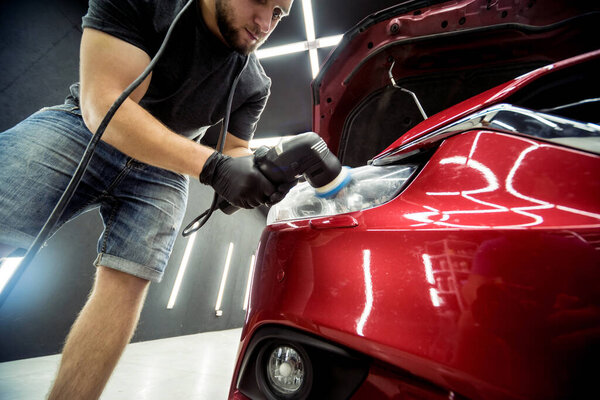 Car service worker polishes a car details with orbital polisher.