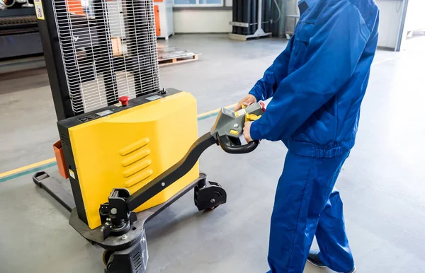 Un trabajador en un almacén utiliza un apilador manual para transportar paletas. — Foto de Stock