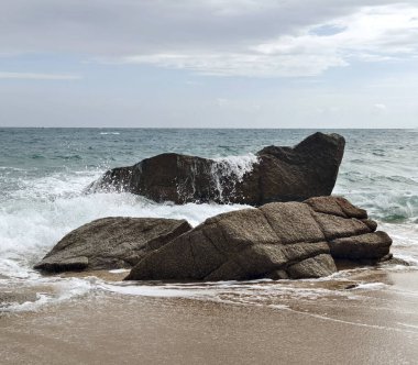 Yumuşak dalgaların kayalara çarptığı sakin bir sahil sahnesi..