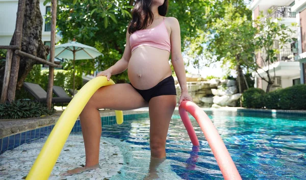 Bilardo oynamak üzere olan hamile genç kadın köpüklü makarnayla havuzda egzersiz yapacak..