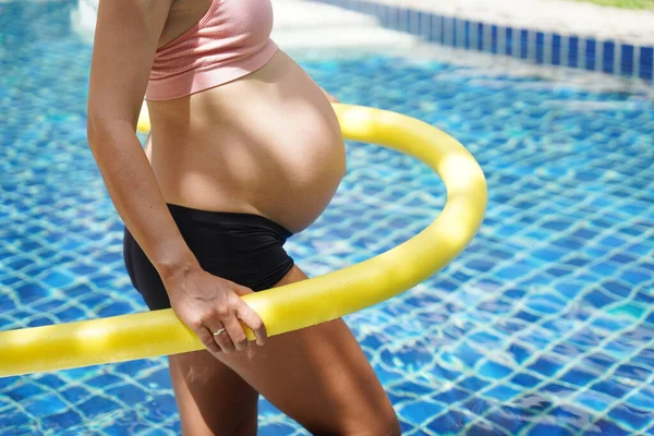 Bilardo oynamak üzere olan hamile genç kadın köpüklü makarnayla havuzda egzersiz yapacak..