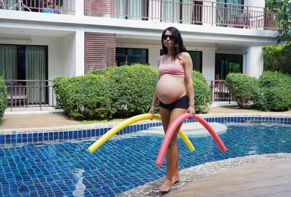 Bilardo oynamak üzere olan hamile genç kadın köpüklü makarnayla havuzda egzersiz yapacak..