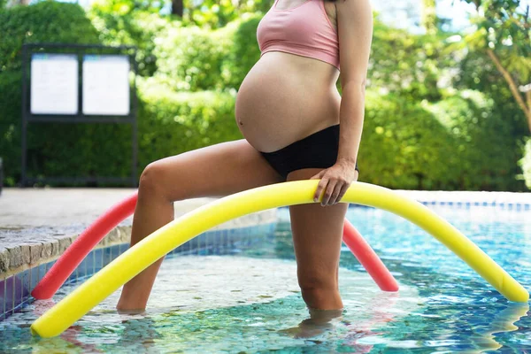 Bilardo oynamak üzere olan hamile genç kadın köpüklü makarnayla havuzda egzersiz yapacak..