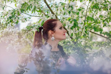 Çekici bir kadın portresi bahar çiçek açan elma ağacının altında bir deri ceket giymiş. Birden fazla poz