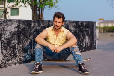 Sokakta longboard üzerinde oturan genç adam.