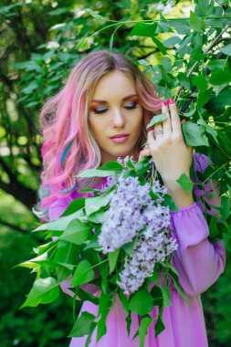 Güzel moda model kızla renkli boyalı saç ve Lila bush ve holding eflatun çiçekler yanında mükemmel makyaj ve saç standig