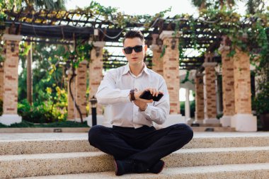 Onun telefon tutarak ve tropikal bir ülkede açık havada merdivenlerde oturan genç işadamı