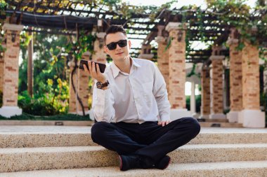 Onun telefon tutarak ve tropikal bir ülkede açık havada merdivenlerde oturan genç işadamı